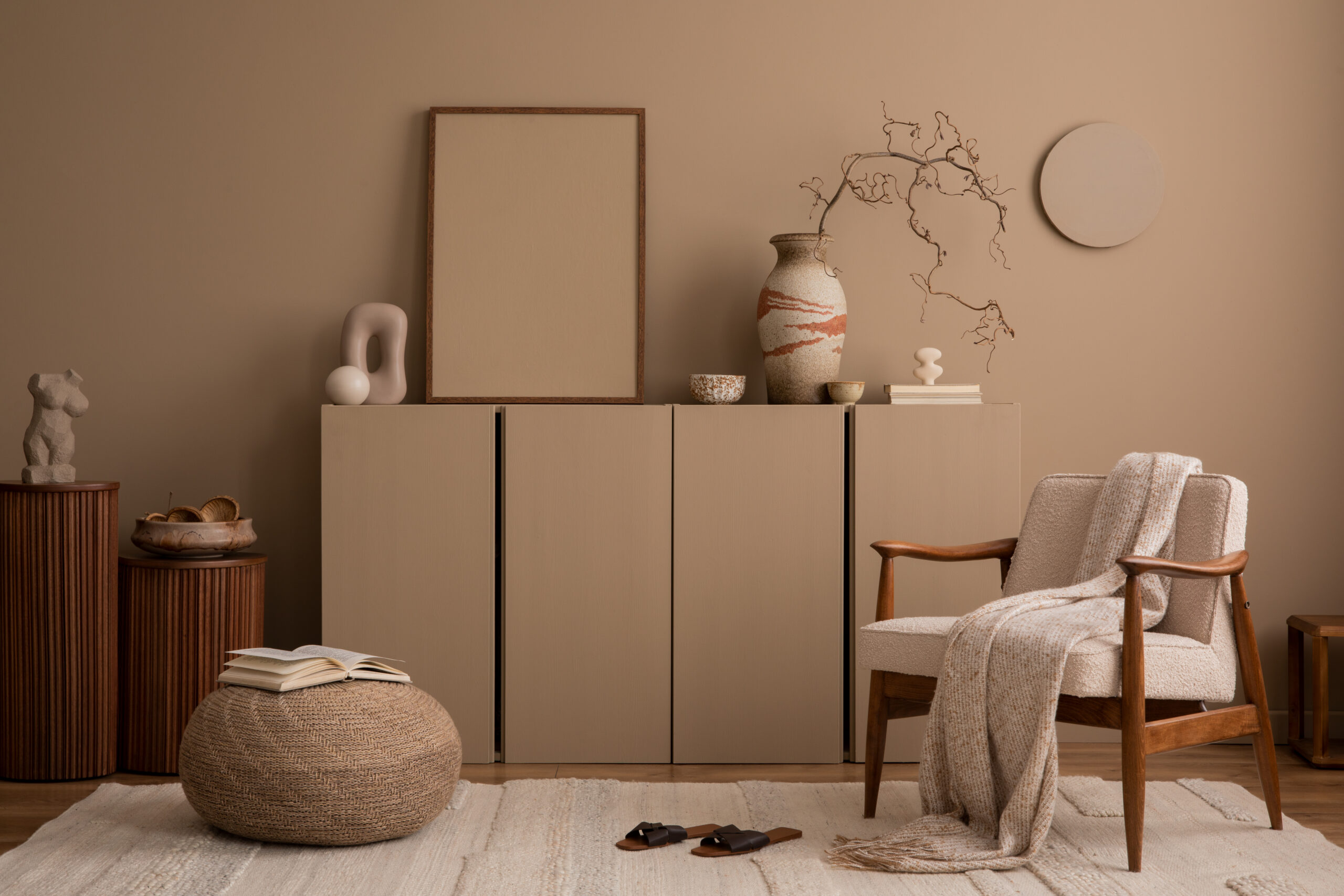 Aesthetics composition of living room interior with mock up poster frame, brown wall, sideboard, boucle armchair, sculpture, braided pouf, plaid and personal accessories. Home decor. Template.